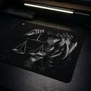 Ângulo para o Mouse Pad Control Gamer Justice V3 posicionado na esquerda da imagem, sua cor é preta com arte ilustrativa em branco e preto de uma figura feminina de cabelos brancos com uma coroa de espinhos, segurando uma balança de pratos. Um teclado mecânico preto está visível no canto superior esquerdo da imagem, em uma mesa de madeira escura iluminada por uma luminária de LED.
