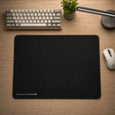 O Mouse Pad Control Gamer Ultrabrake em uma mesa de jogo, com um teclado e mouse gamer. Esta imagem mostra o mouse pad em ação, posicionado em uma mesa de madeira texturizada. A luminária LED articulada e a pequena planta no vaso em segundo plano sugerem um setup de jogo limpo e organizado. O mouse pad se integra perfeitamente ao ambiente, com o logotipo "ULTRABRAKE XL" visível no canto inferior esquerdo. As bordas costuradas e a superfície preta texturizada do mouse pad são claramente visíveis.