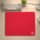 Visão superior do Mouse Pad Gamer Ultraerialace vermelho centralizado em uma mesa de madeira clara. O amplo espaço para jogos é demonstrado no setup, que inclui teclado, planta, luminária e um mouse branco posicionado fora do pad, à direita.