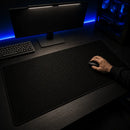 Mão de uma pessoa utilizando um mouse preto sobre o Mouse Pad Grande Gamer Ondas Escuras. O produto está estendido em uma mesa escura de setup gamer, iluminado por uma lightbar de monitor, com luzes LED azuis ao fundo.