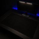 Perspectiva lateral do Mouse Pad Grande Gamer Ondas Escuras em um setup gamer minimalista. A luz suave da lightbar do monitor reflete levemente sobre a superfície preta do mouse pad, evidenciando seu tamanho grande e acabamento premium.