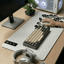 Visão oblíqua de um setup gamer clean com Mouse Pad Grande Gamer Sakura estendido sobre mesa de madeira clara. Sobre o mouse pad, um teclado mecânico compacto e um mouse branco sendo utilizado. Ao fundo, um gabinete de PC branco com iluminação RGB, um monitor e um pequeno bonsai decorativo.