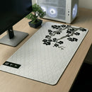 Mouse Pad Grande Gamer Sakura posicionado em uma mesa de madeira clara, destacando a estampa de ondas japonesas e o galho de cerejeira negra. A imagem mostra o produto em destaque, enfatizando o amplo espaço para teclado e mouse, com um gabinete gamer branco e um bonsai ao fundo.