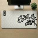 Visão superior de um Mouse Pad Grande Gamer Sakura (90x40cm) centralizado em uma mesa de madeira. A foto destaca a estampa completa de ondas estilo Seigaiha e o galho de cerejeira negra, com a base de um monitor e um pequeno bonsai posicionados simetricamente na parte superior.
