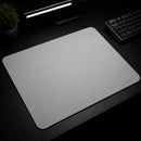 Uma foto em ângulo lateral e frontal do Mouse Pad Pk Control Gamer branco, realçando a textura da superfície de tecido e a nitidez das bordas costuradas brancas. O logotipo "PK CONTROL I" é claramente visível no canto inferior direito, e a base de borracha texturizada antiderrapante é ligeiramente visível no canto inferior esquerdo. O teclado mecânico cinza e a luminária preta estão desfocados ao fundo.