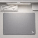 Vista superior do Mouse Pad Speed Gamer Galaxy Gem na cor cinza com textura suave e logo branca no canto inferior direito do produto. O mouse pad repousa sobre uma mesa clara em um setup minimalista, posicionado abaixo de um teclado mecânico branco e uma barra de luz.