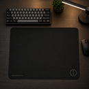 Visão superior em um ângulo levemente diferente do mouse pad Ultradash de 450x400mm. O design minimalista e a base de borracha firme ficam em destaque no centro da mesa com iluminação quente da luminária ao fundo.