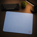 Mouse Pad Gamer Speed Ultradash Blue exibido sobre uma mesa de madeira iluminada por uma luminária. A imagem destaca a base firme de borracha e a superfície de tecido azul suave, evidenciando o acabamento do logotipo e das bordas costuradas no ambiente gamer.