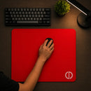 Vista aérea de um setup gamer minimalista mostrando o Mouse Pad Speed Gamer Ultradash Red em uso. Uma mão segura um mouse preto sobre a superfície lisa de tecido vermelho. Na parte superior, há um teclado mecânico compacto e, ao lado, uma luminária de mesa acesa com luz quente.