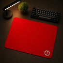 Perspectiva lateral do Mouse Pad Speed Gamer Ultradash Red em um ambiente profissional e imersivo. O mouse pad vermelho retangular ocupa a maior parte da imagem sobre uma superfície escura, com o logotipo branco em evidência e um teclado compacto ao fundo sob a luz direcionada de uma luminária de LED.